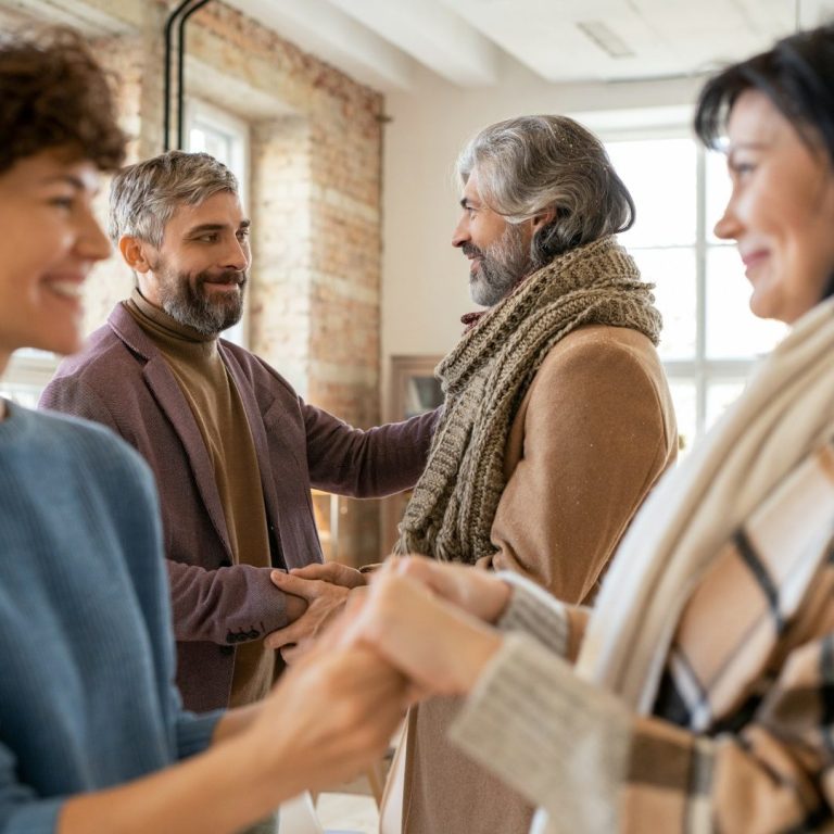 Four people greet each other warmly in a bright, cozy indoor setting.