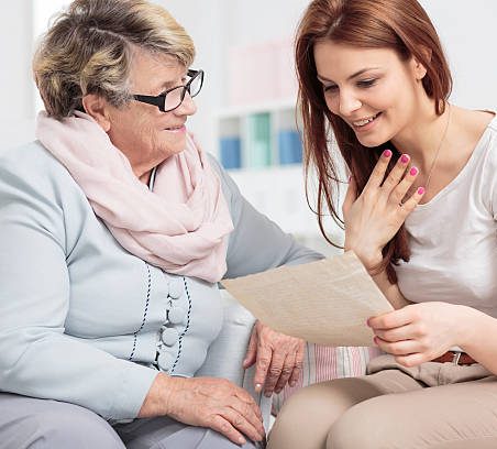 An older woman and a young woman smile while reading a letter together.