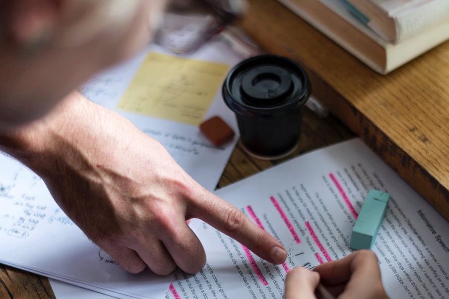 A hand pointing at highlighted text on papers with a coffee cup nearby.