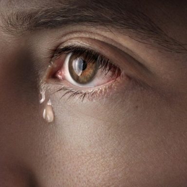 Close-up of a brown eye with a single tear rolling down the cheek.
