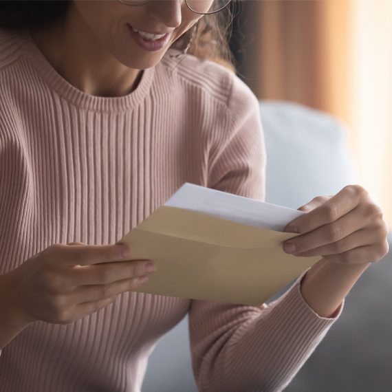 Woman smiling while holding an envelope and a letter indoors.