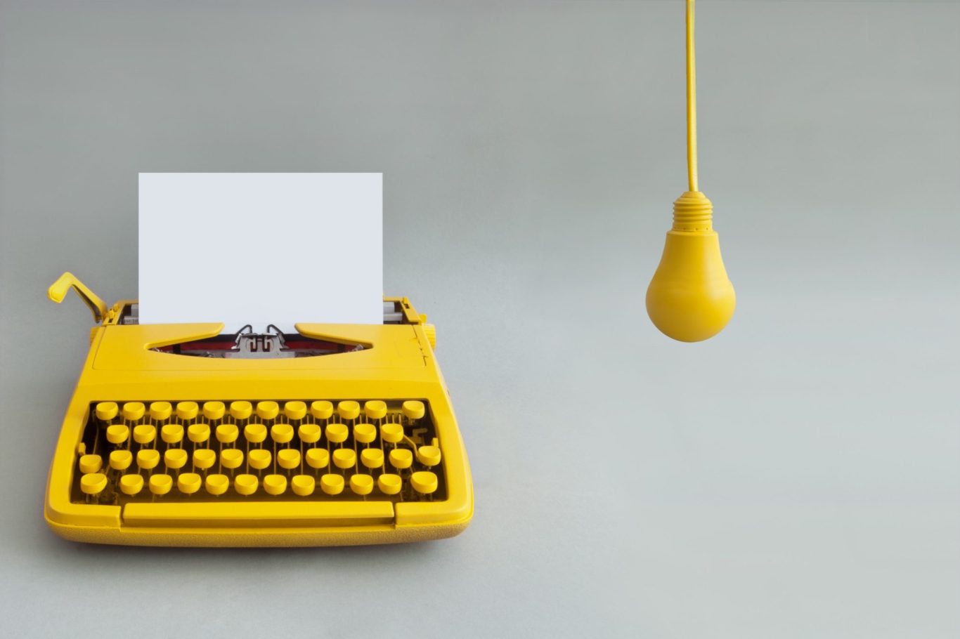 Yellow typewriter with a blank sheet of paper and a hanging yellow light bulb.