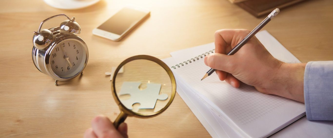 Birch & Ink — Research Services A hand holds a pen over a notebook, with a magnifying glass and alarm clock nearby.