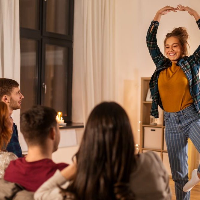A woman performs charades joyfully for a small group in a cozy indoor setting.