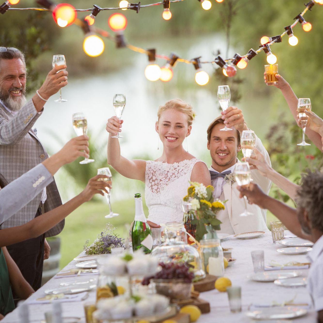 A group of guests toasting at a wedding reception outdoors, surrounded by string lights.