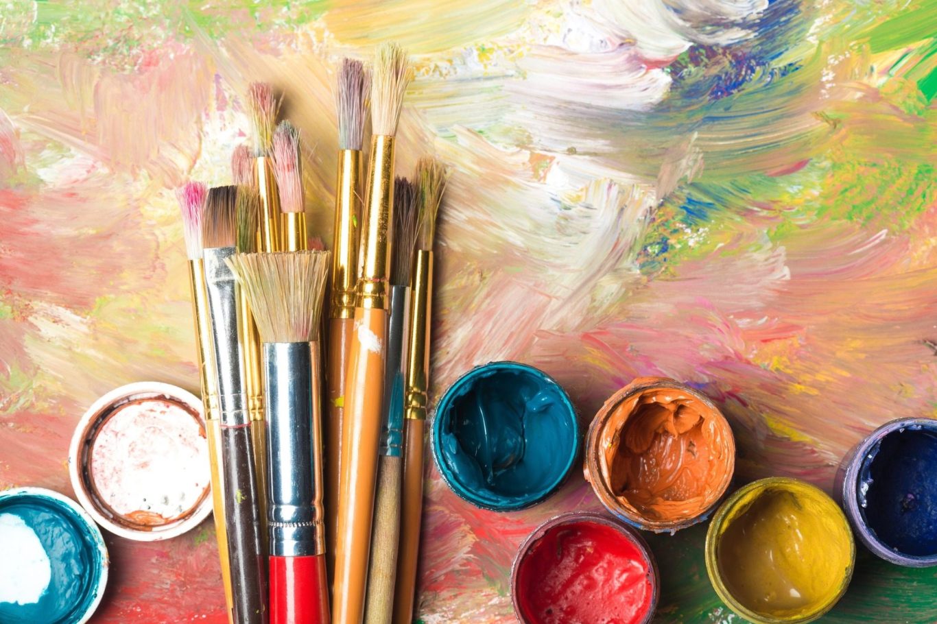 Assorted paintbrushes and vibrant acrylic paints on an abstract background.