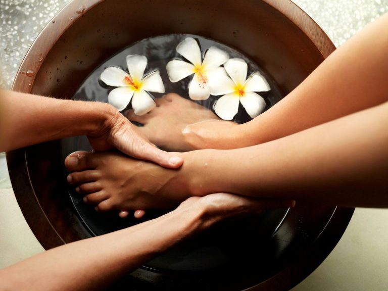 Pedicures at Birch and Ink Retreat Hands gently massaging feet in a bowl of water with floating flowers.