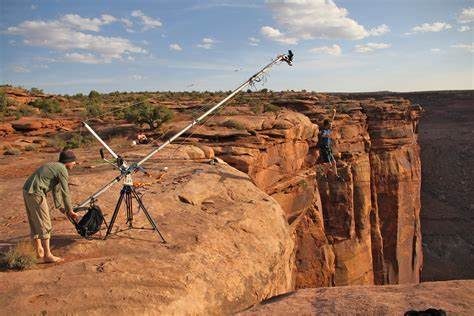 A person operates equipment near a canyon edge under a blue sky with clouds.