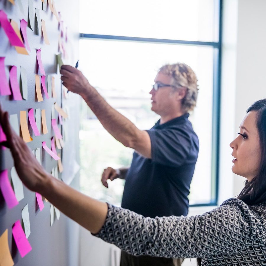 Two people collaborating by arranging colorful sticky notes on a wall.