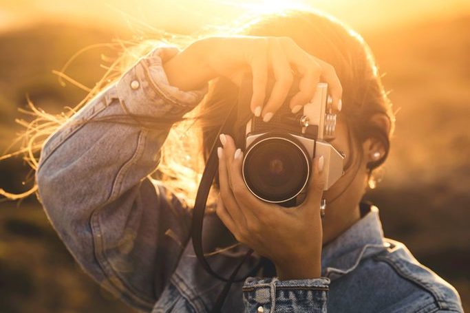 Person holding a camera and taking a photo against a golden sunset backdrop.