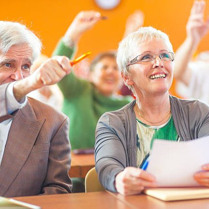 Elderly people in a classroom raising hands, smiling, and engaged in a discussion.