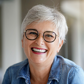 Smiling woman with short gray hair and glasses, wearing a denim shirt.