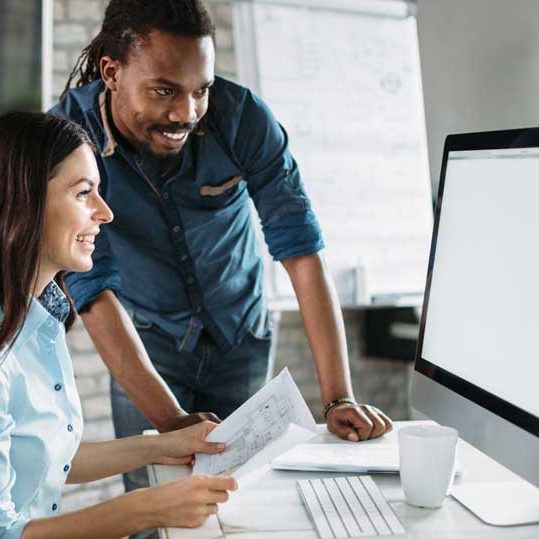 Two colleagues reviewing content together at a desk, smiling and engaged.