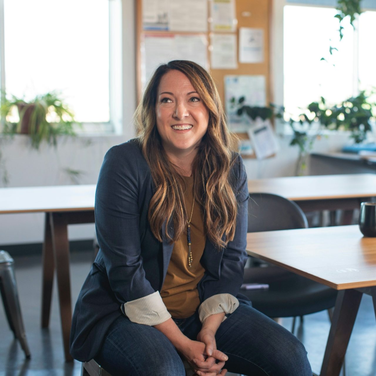 Smiling woman sitting at a table in a bright, plant-filled room.