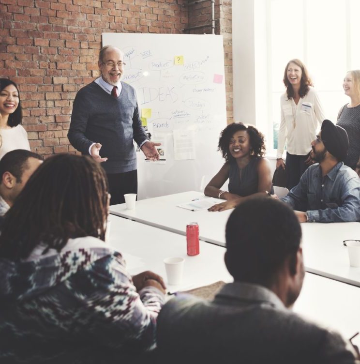 A diverse group of people in a class, listening to a speaker in a bright, modern room.