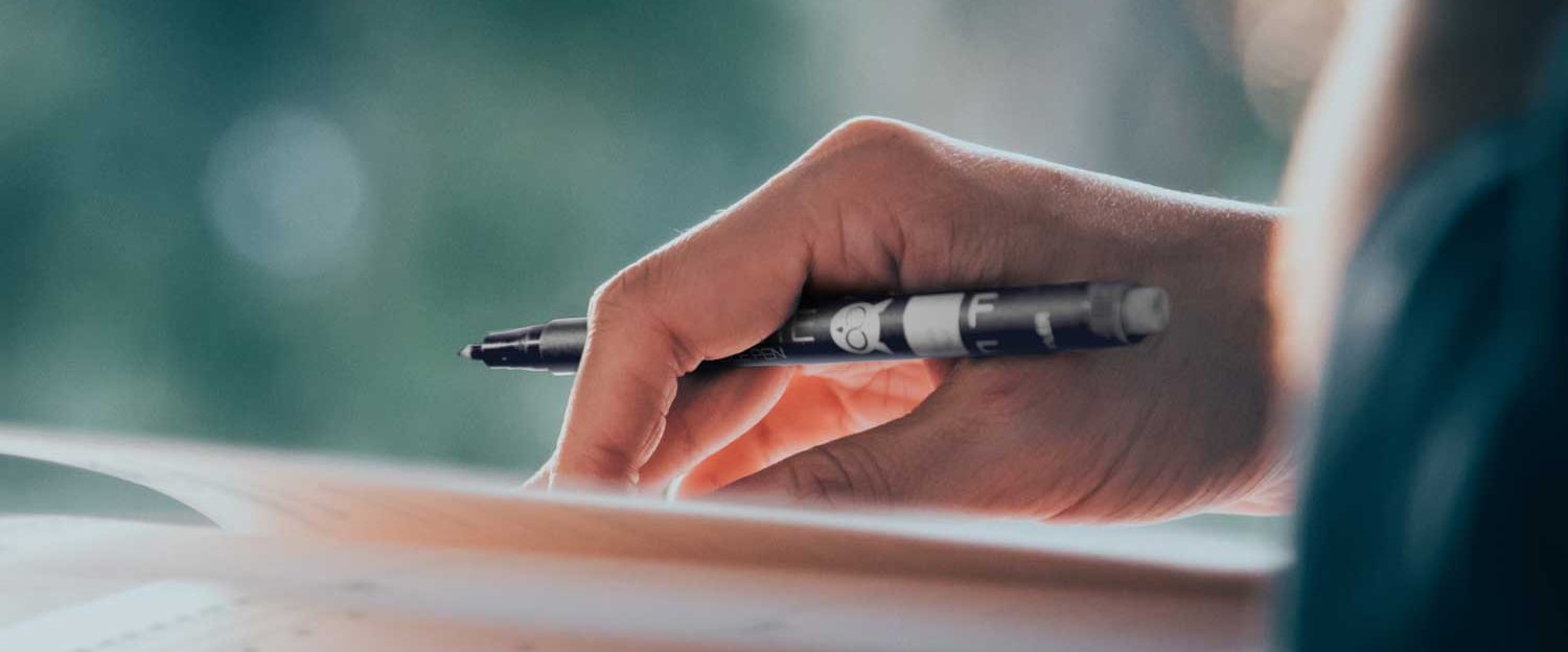A hand holding a pen, poised over a sheet of paper.