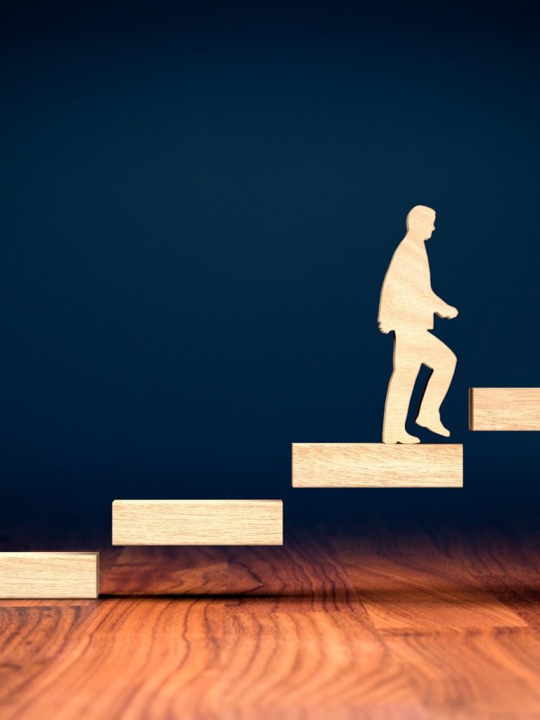 Silhouette of a person ascending wooden steps against a dark background.