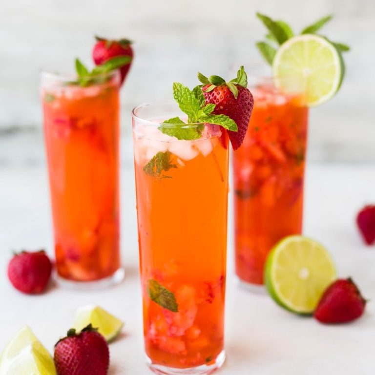 Three tall glasses of vibrant strawberry drinks, garnished with mint and lime slices.