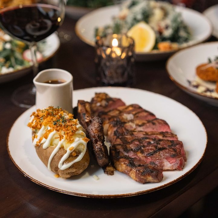 Grilled steak with a loaded baked potato and dipping sauce, garnished with herbs.