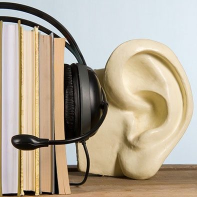 Headphones resting on a stack of books beside a large ear sculpture.