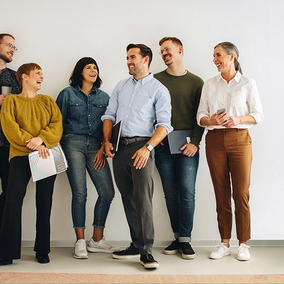 Group of six professionals smiling and chatting in a bright, modern office space.