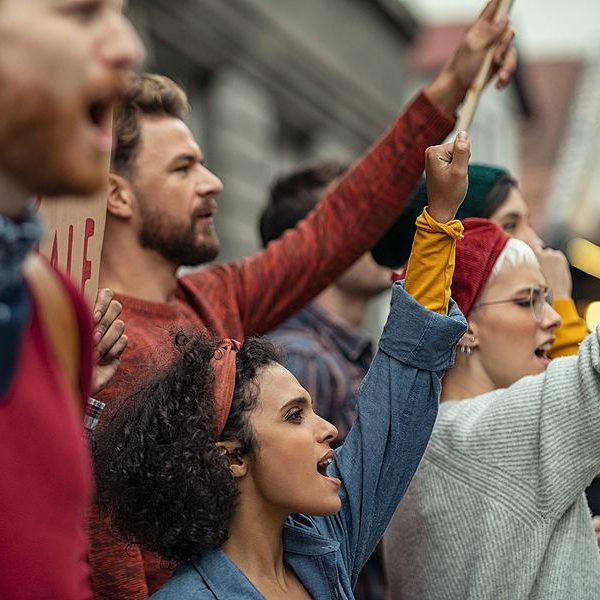 A diverse group of people participating in a protest, raising their fists and chanting.