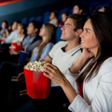 A diverse group of moviegoers enjoying a film with popcorn in a theater.