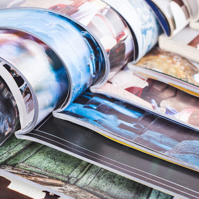 A stack of magazines displaying various colorful images and text on glossy pages.